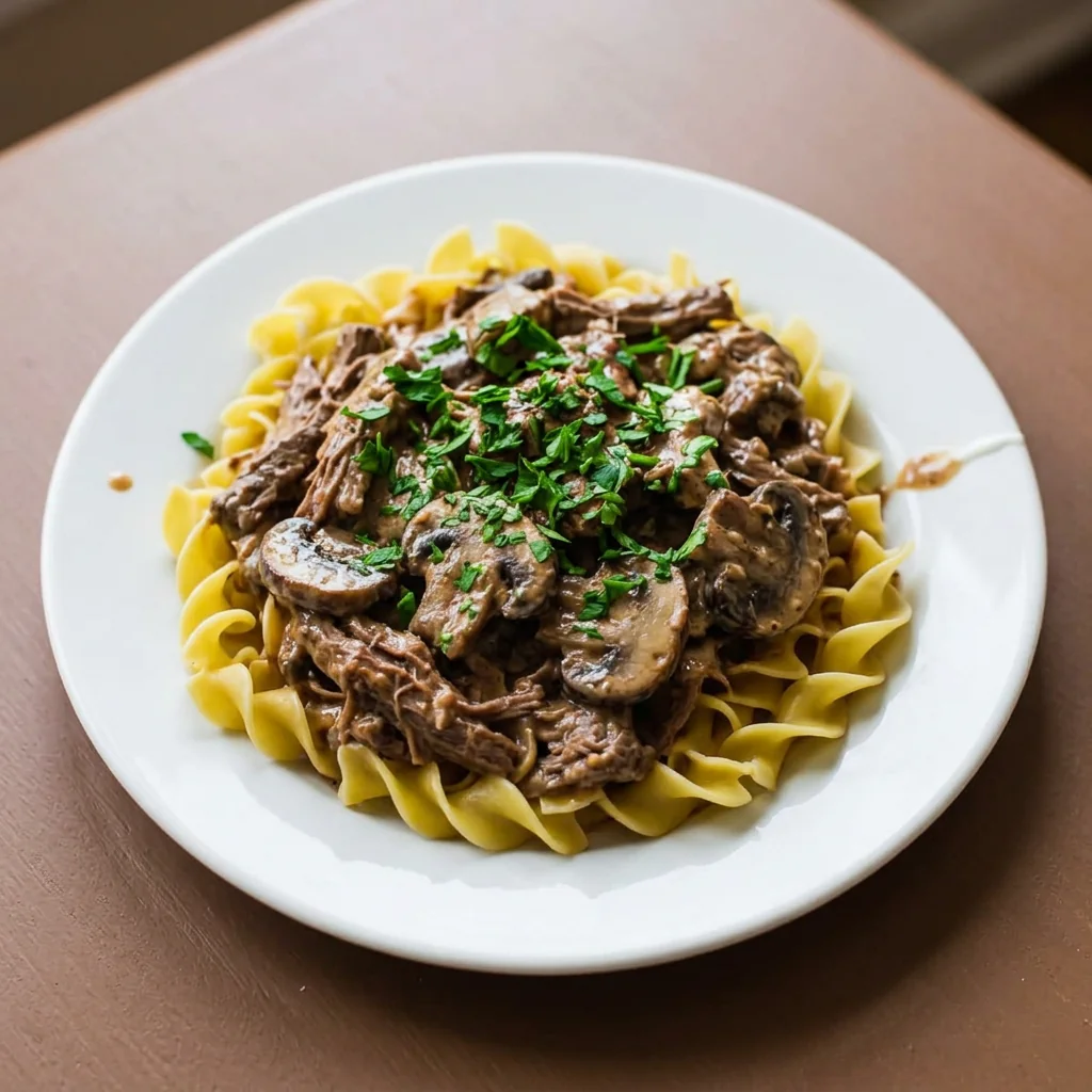 Beef stroganoff with mushrooms in creamy sauce over egg noodles on a white plate