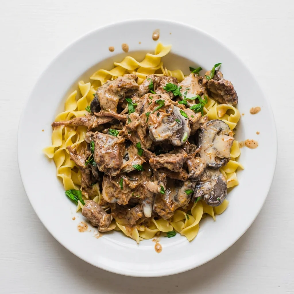 Overhead view of beef stroganoff over egg noodles in a white bowl